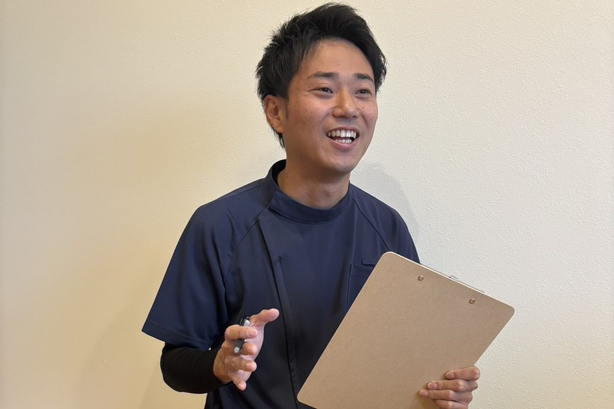 クリップボードとペンを手に、笑顔で話をする安井先生