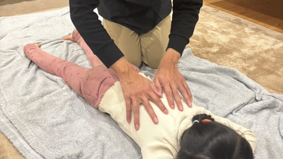 うつぶせのお子さまの背中に、安井先生が両手を当ててマッサージしている様子