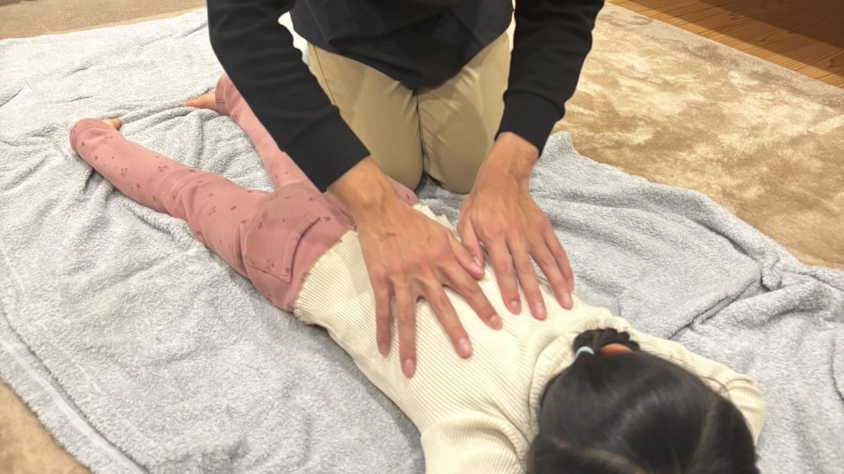 タオルの上でうつぶせになったお子さまの背中に、安井先生が両手を添えている様子