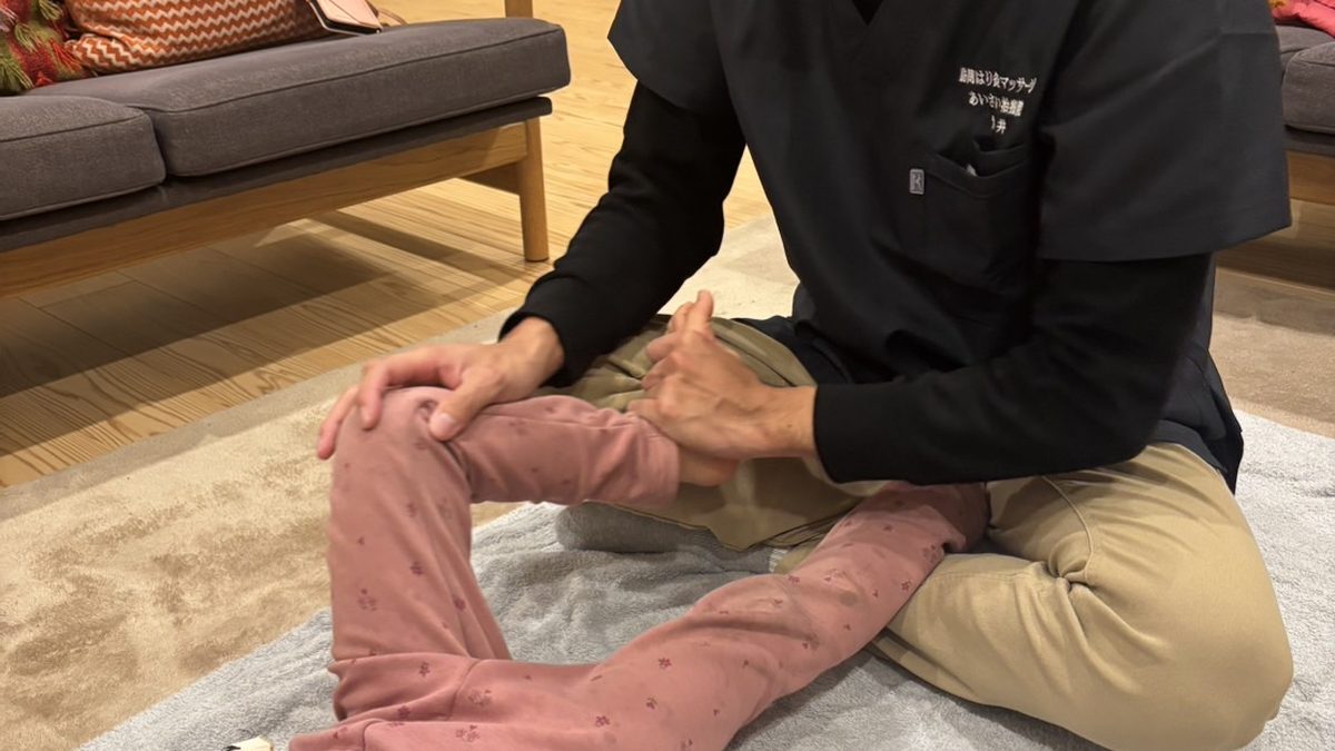 床に座った安井先生が、お子さまの膝に手を添えて脚を支えている様子
