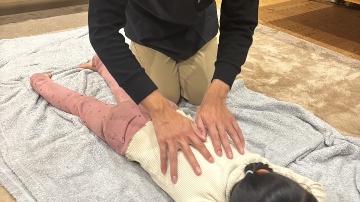 うつぶせのお子さまの背中に、安井先生が両手を当ててマッサージしている様子
