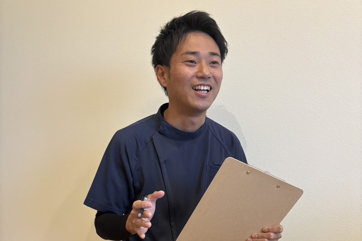 クリップボードを手に、笑顔で話をする安井先生